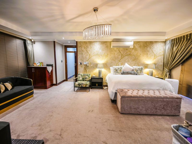 Spacious bedroom featuring a wall-mounted air conditioning unit, decorative wallpaper, recessed ceiling lighting, and fitted carpeting with large windows covered by venetian blinds.