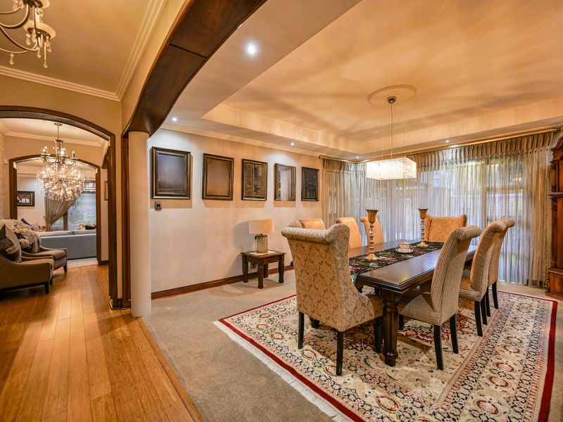 Elegant dining room featuring a recessed ceiling with cove lighting, hardwood and carpet flooring, and a classic archway leading to an adjacent living space.