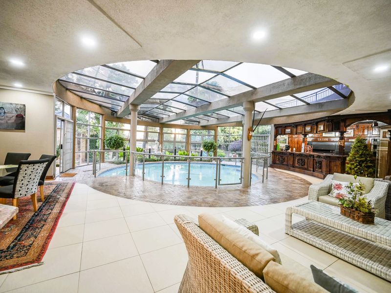 An impressive indoor pool area featuring a glass atrium roof, tiled flooring, a built-in bar, and a modern glass balustrade surrounding the pool.