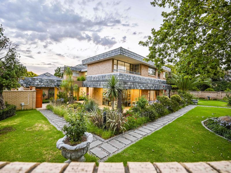 A well-maintained two-story brick residence featuring a distinctive slate-tiled roof, surrounded by a lush landscaped garden with paved walkways and a private balcony.