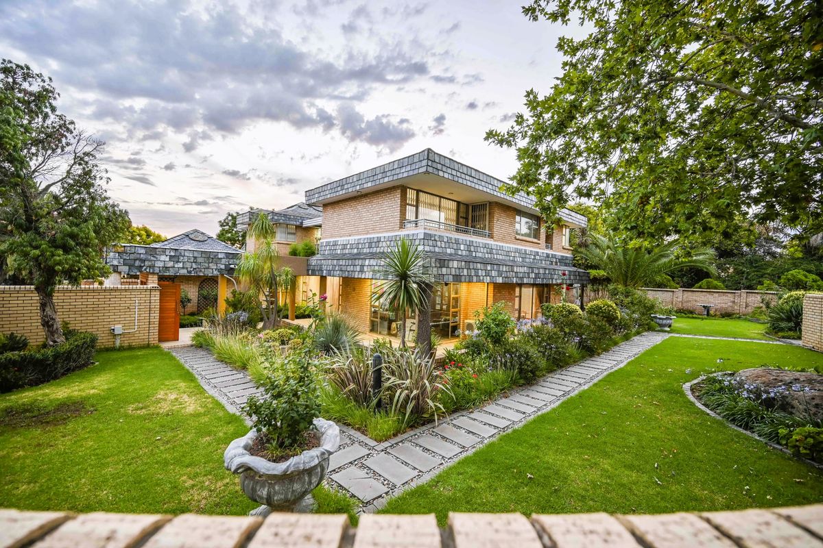 A well-maintained two-story brick residence featuring a distinctive slate-tiled roof, surrounded by a lush landscaped garden with paved walkways and a private balcony.