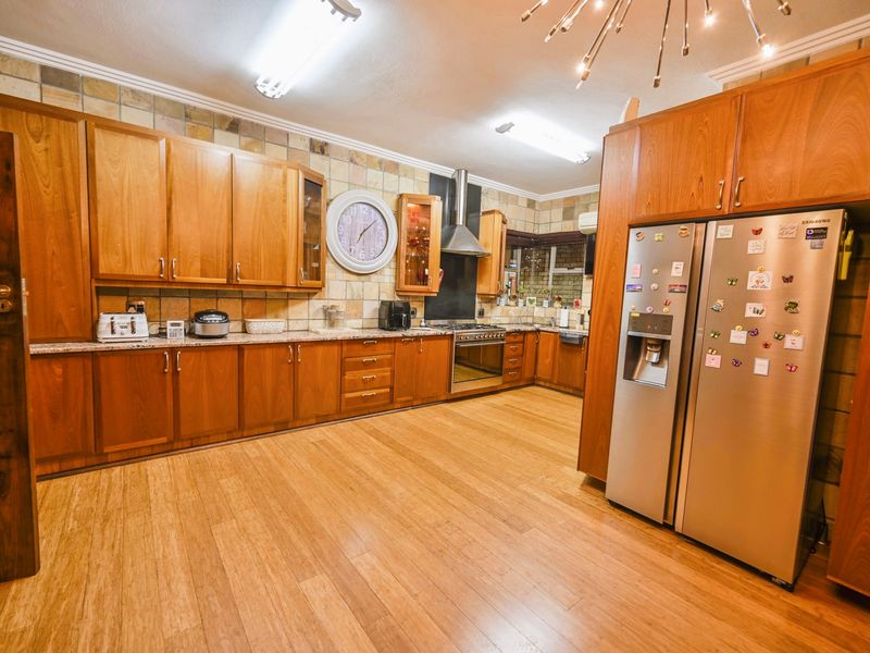 Spacious kitchen featuring extensive wooden cabinetry, granite countertops, a built-in oven with extractor fan, and durable laminate flooring.