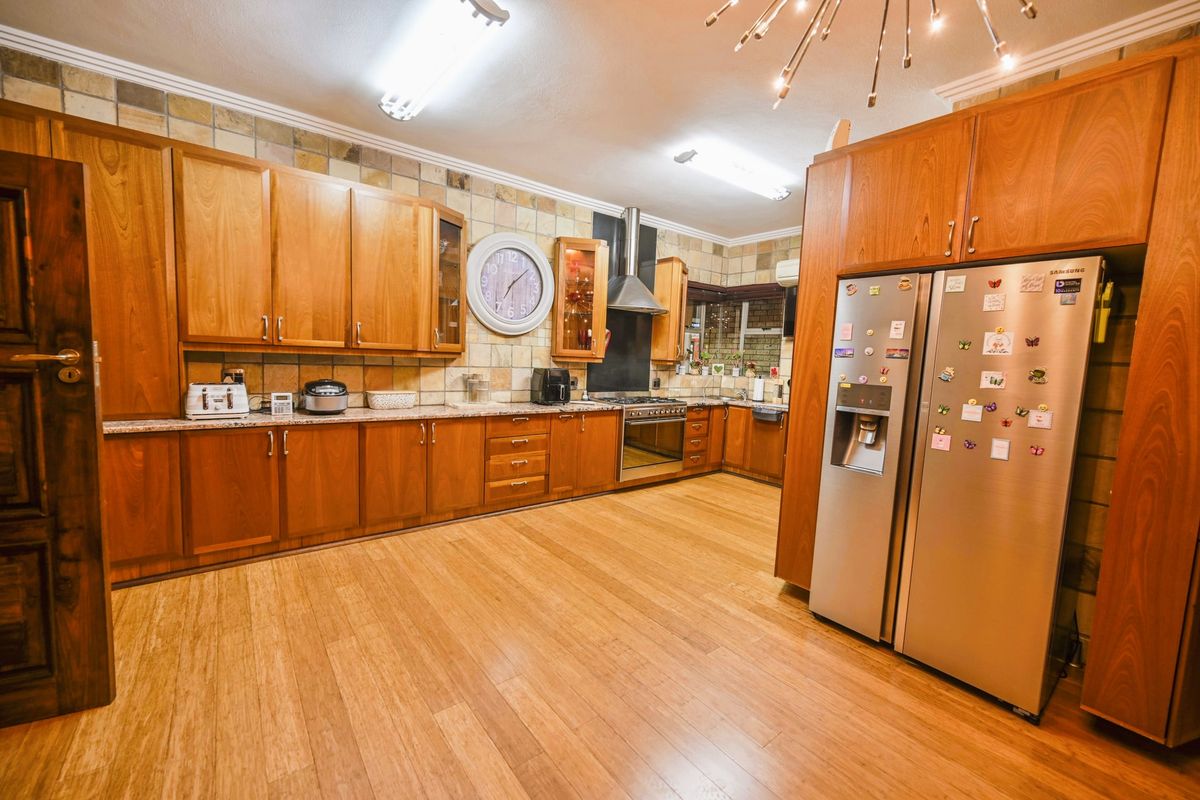 Spacious kitchen featuring extensive wooden cabinetry, granite countertops, a built-in oven with extractor fan, and durable laminate flooring.