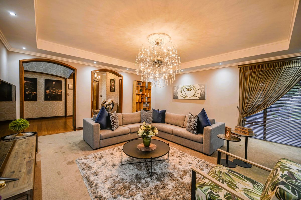A well-appointed living room featuring a decorative crystal chandelier, recessed ceiling lighting, and an elegant arched entryway leading to an adjacent space.