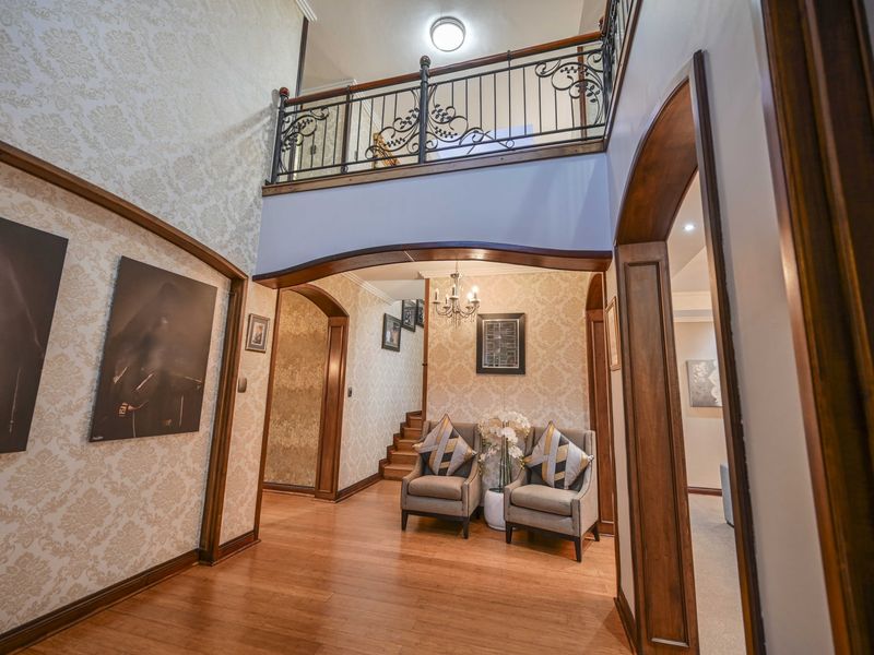Spacious double-volume entrance hall featuring hardwood flooring, elegant arched doorways, and a decorative wrought iron balustrade overlooking the landing.