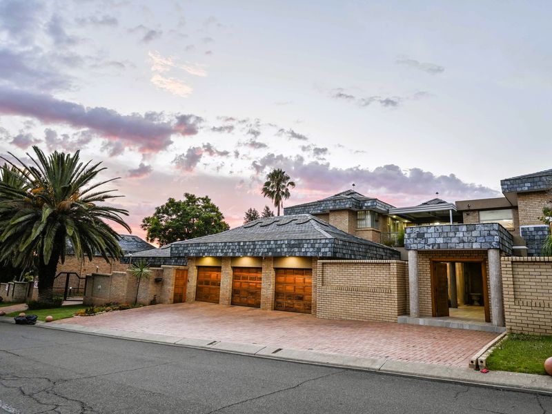 Front elevation of a substantial residence featuring a triple garage, brick construction, slate roof tiles, and a paved driveway at dusk.