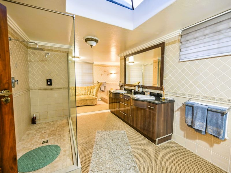 Spacious bathroom featuring a double vanity with granite countertops, a large glass-enclosed shower, and a skylight providing natural light.