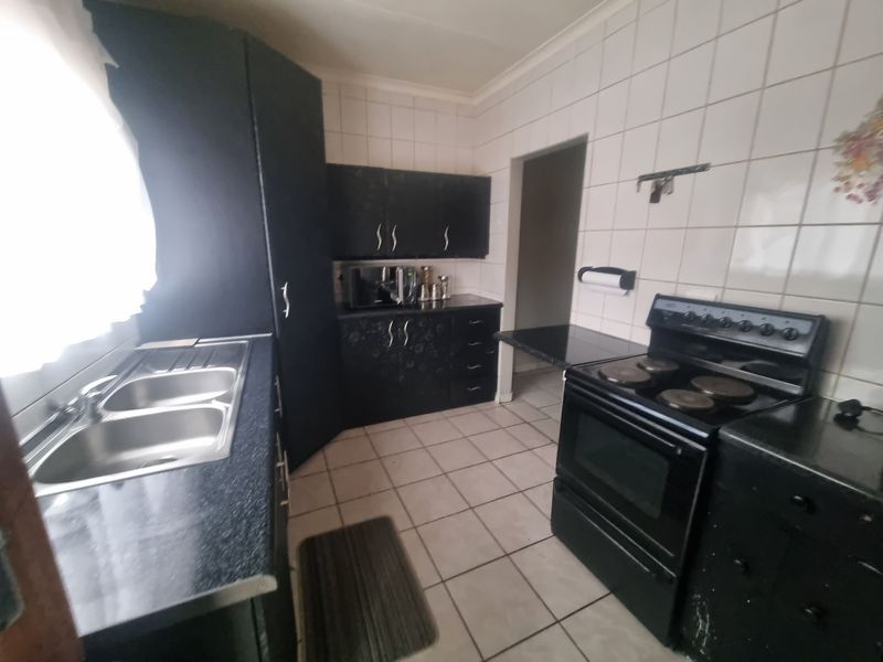 A functional kitchen featuring dark cabinetry, laminate countertops, a double bowl sink, and a freestanding electric stove with tiled walls and flooring.