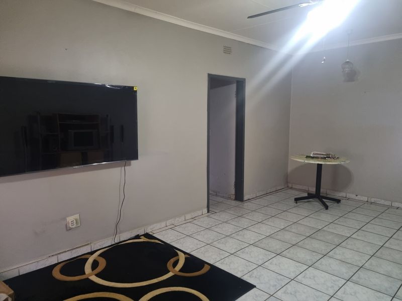 A sparsely furnished living area featuring neutral wall tones, tiled flooring, and a ceiling fan, offering a blank canvas for personalization.