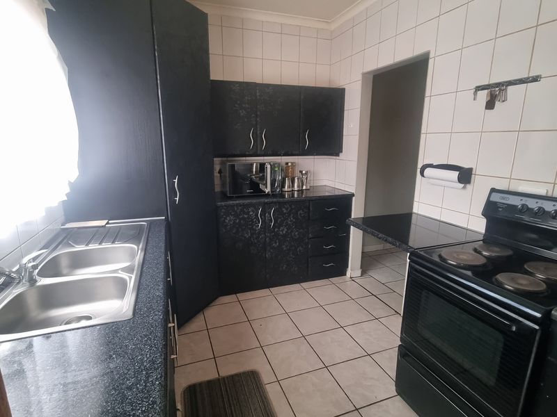 A functional kitchen featuring dark cabinetry, laminate countertops, a double bowl sink, and a freestanding electric stove with tiled splashbacks and flooring.