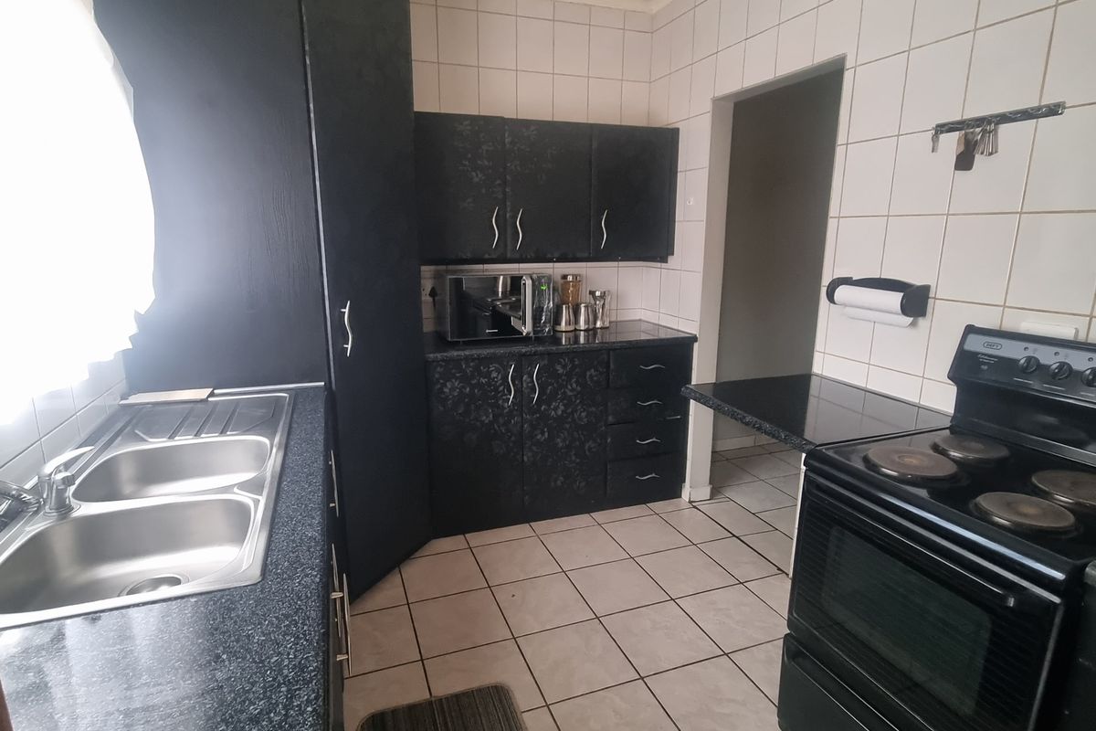 A functional kitchen featuring dark cabinetry, laminate countertops, a double bowl sink, and a freestanding electric stove with tiled splashbacks and flooring.