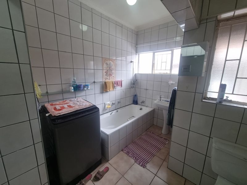 A functional bathroom featuring a bathtub, pedestal basin, and toilet, finished with full-height wall tiling and floor tiles.