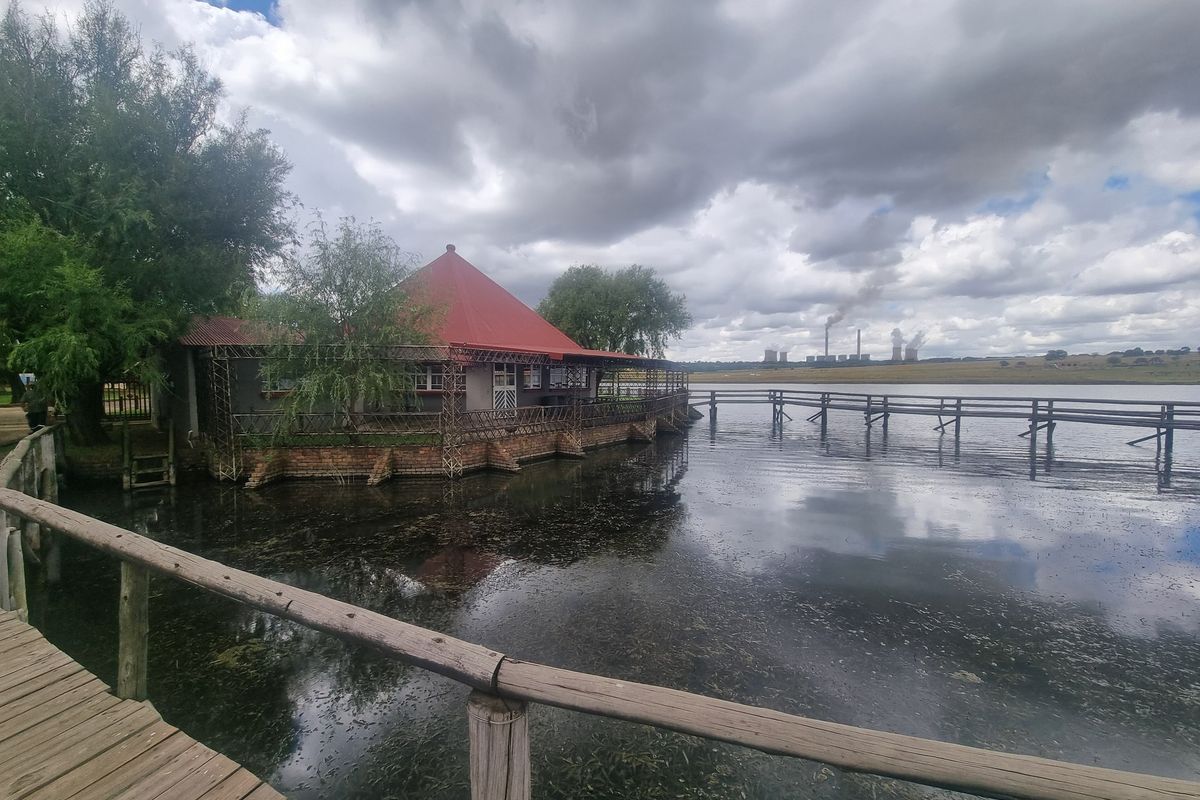 A waterfront property featuring a structure with a red metal roof, connected by a wooden walkway over the water.