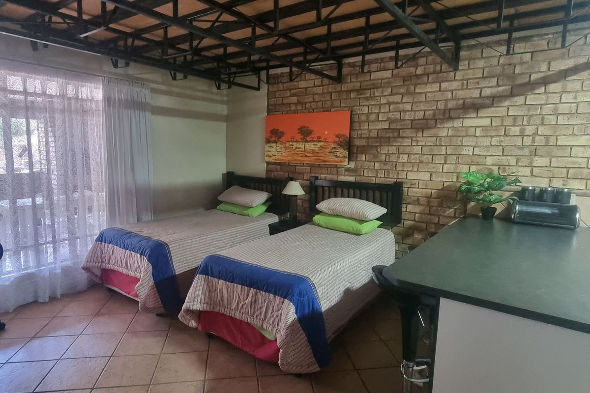 Bedroom featuring exposed steel roof trusses, a facebrick feature wall, tiled flooring, and direct access to an outdoor area via a sliding glass door.