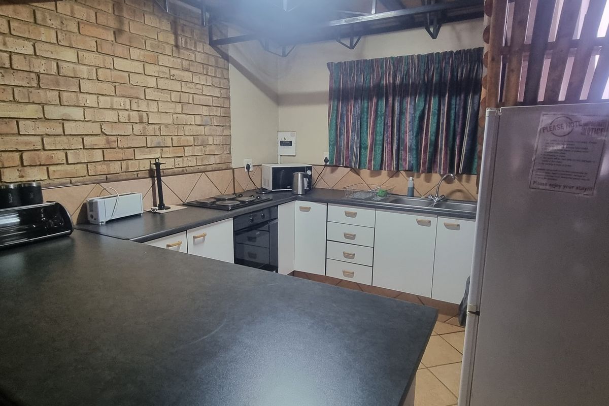 A functional kitchen featuring exposed brick walls, dark laminate countertops, built-in oven and hob, and a double basin sink with tiled backsplash.