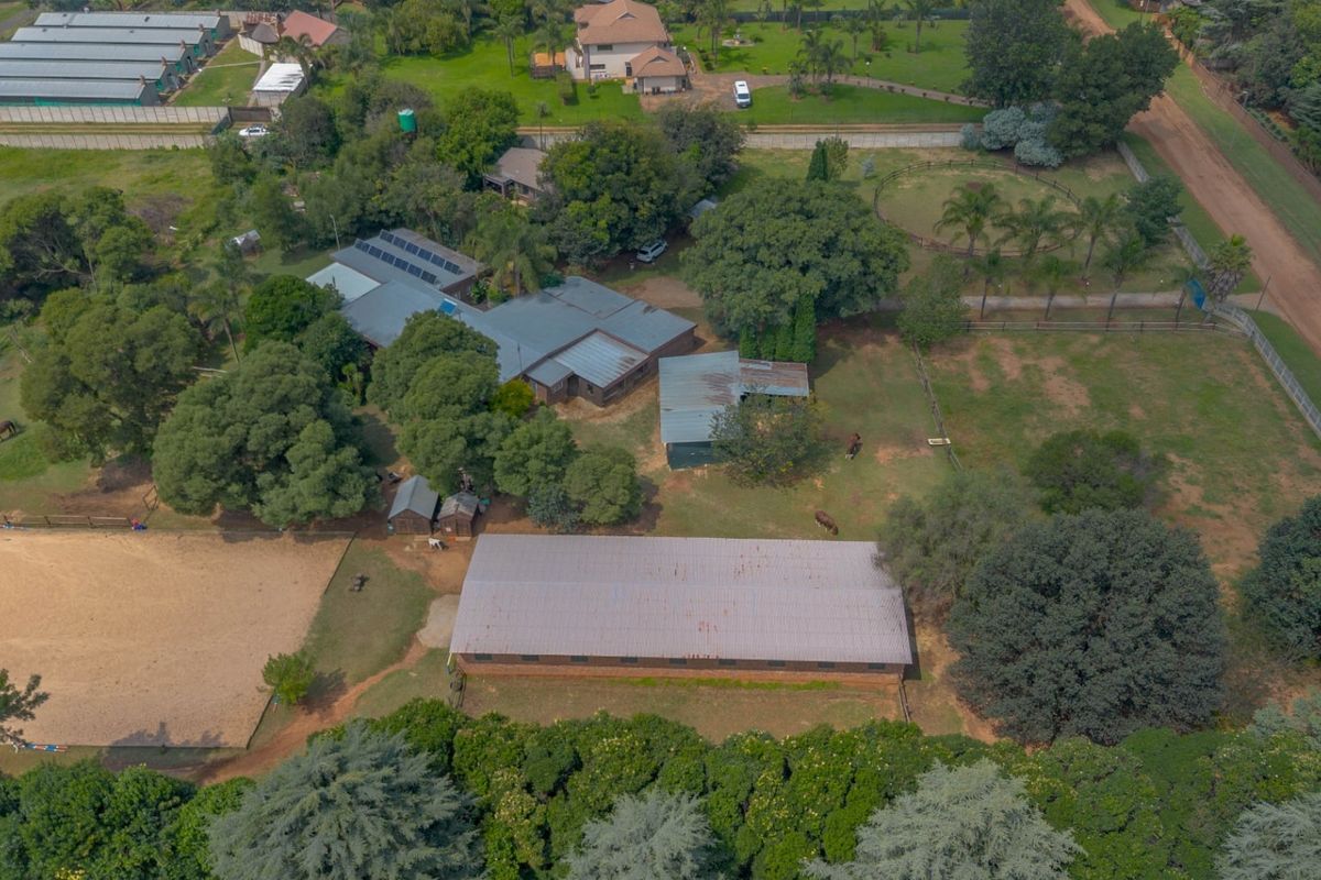 Aerial view of a large property featuring multiple buildings, a metal-roofed stable block, an equestrian arena, and extensive landscaped grounds.
