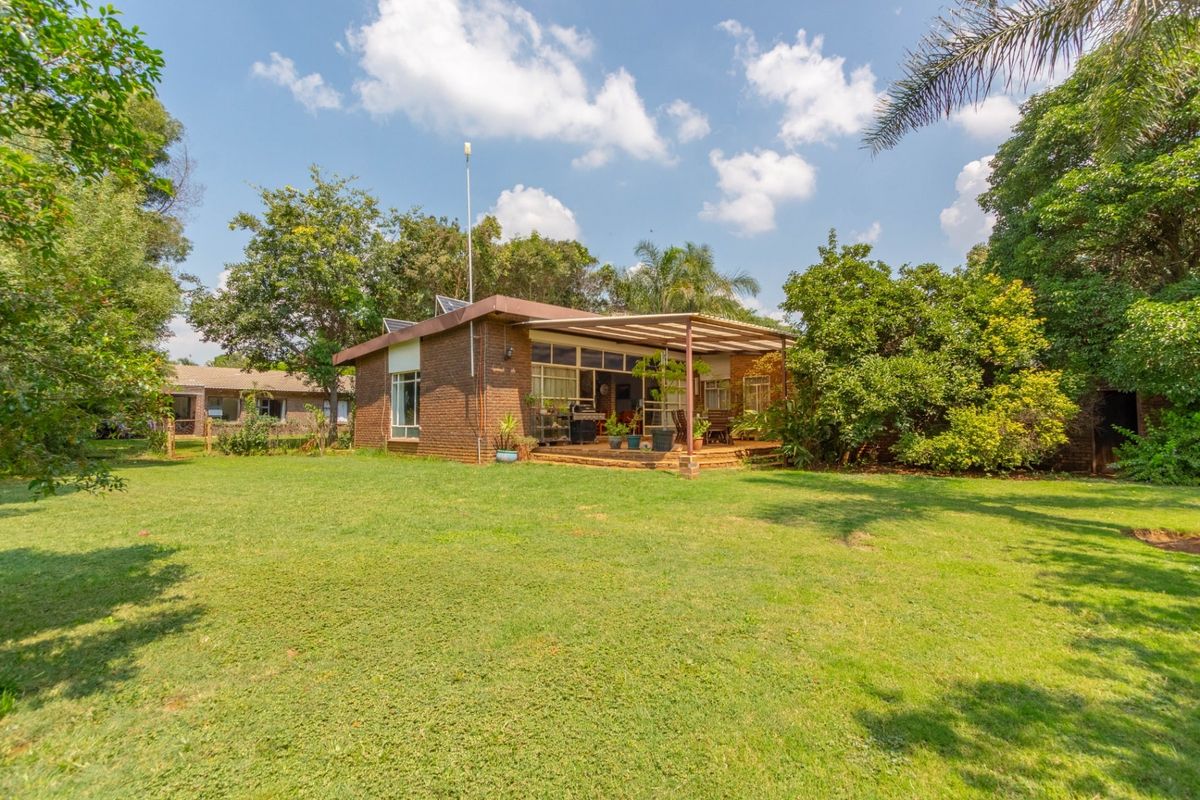 A rear view of a brick house featuring a covered patio area overlooking a spacious, well-maintained garden with mature trees.