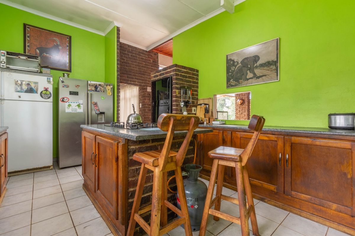 A rustic kitchen featuring wooden cabinetry, a brick-based island with a gas hob, stone countertops, and vibrant green walls with tiled flooring.