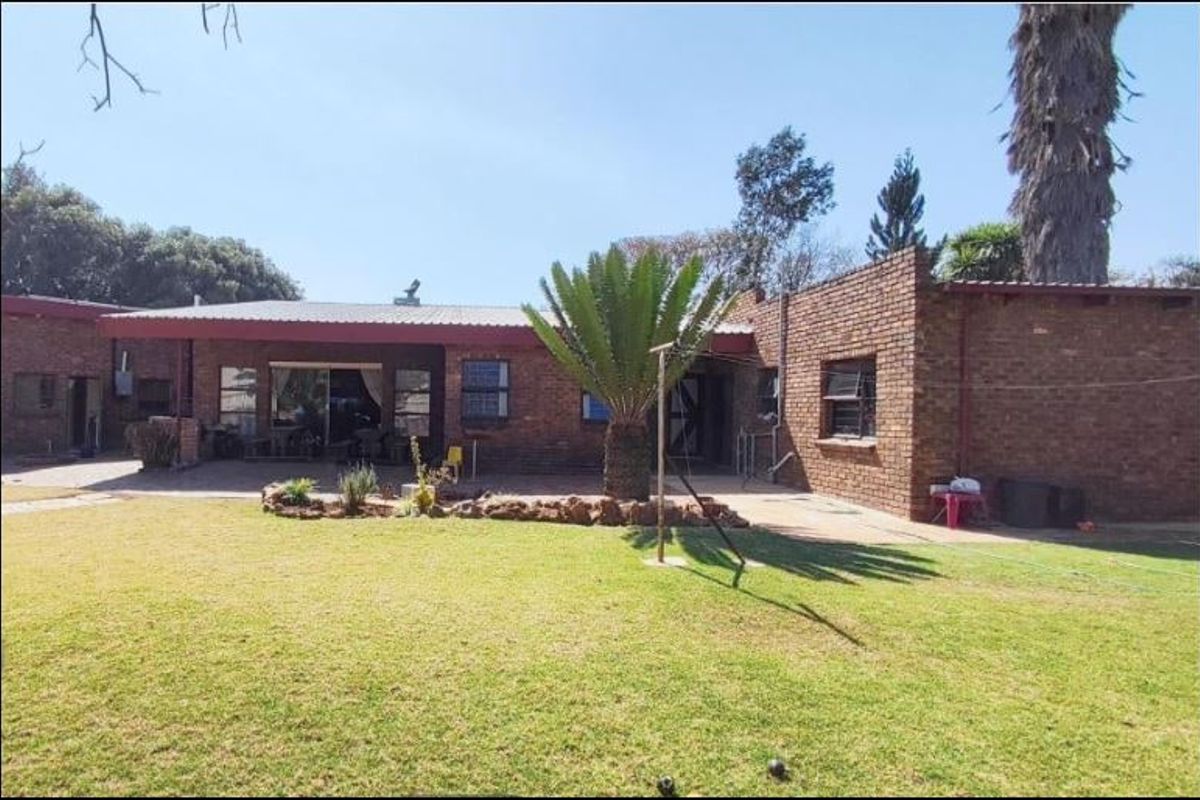 Rear view of a face brick house featuring a covered patio area, sliding glass doors, and a spacious lawn.