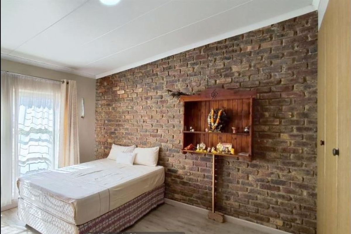A bedroom featuring an exposed brick feature wall, built-in wardrobe storage, and light-toned laminate flooring with access to natural light.