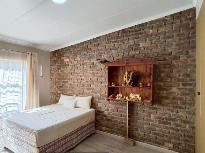 A bedroom featuring an exposed brick feature wall, built-in wardrobe storage, and light-toned laminate flooring with access to natural light.