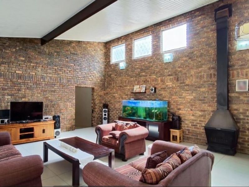 Spacious living room featuring high vaulted ceilings, exposed brick walls, and a prominent freestanding fireplace, creating a warm and character-filled atmosphere.