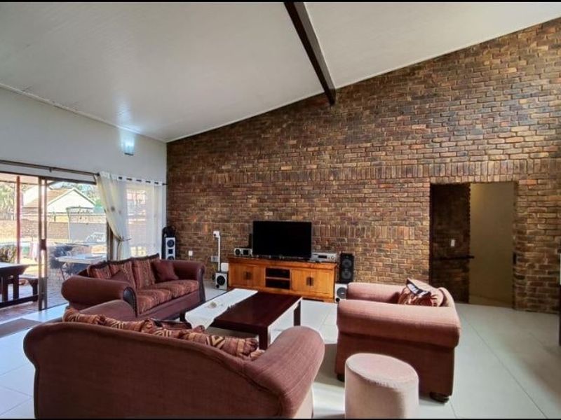 Spacious living room featuring a striking exposed brick feature wall, vaulted ceilings, and large sliding glass doors providing access to the outdoor patio area.