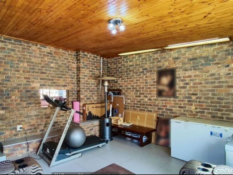 Living area featuring rustic exposed brick walls and a warm timber tongue and groove ceiling with tiled flooring throughout.