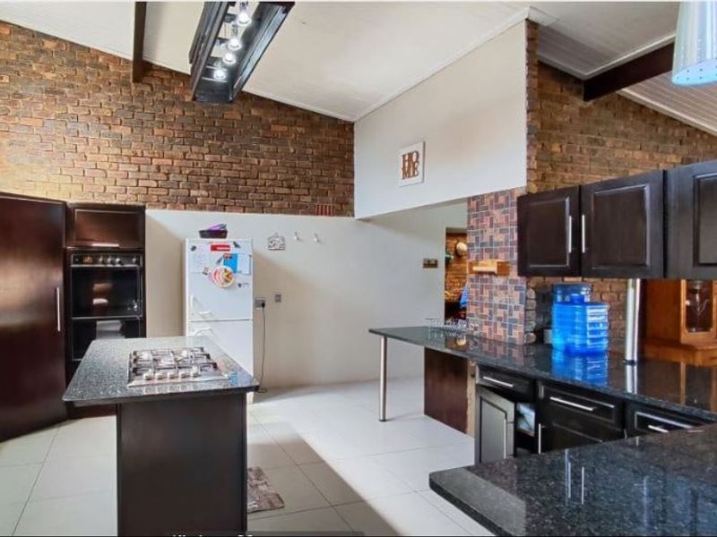 Spacious kitchen featuring exposed brick walls, vaulted ceilings, dark wood cabinetry, granite countertops, and a central island with a built-in gas hob.