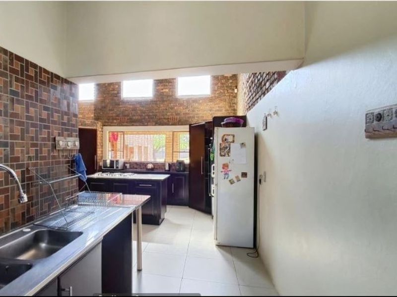 A functional kitchen featuring exposed brick walls, tiled splashbacks, ample cabinetry, and a double sink with a modern mixer tap.