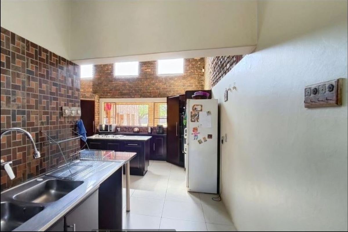 A functional kitchen featuring exposed brick walls, tiled splashbacks, ample cabinetry, and a double sink with a modern mixer tap.