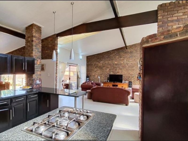 Spacious open-plan living area featuring a modern kitchen with granite island, gas hob, vaulted ceilings with exposed beams, and rustic brick feature walls.