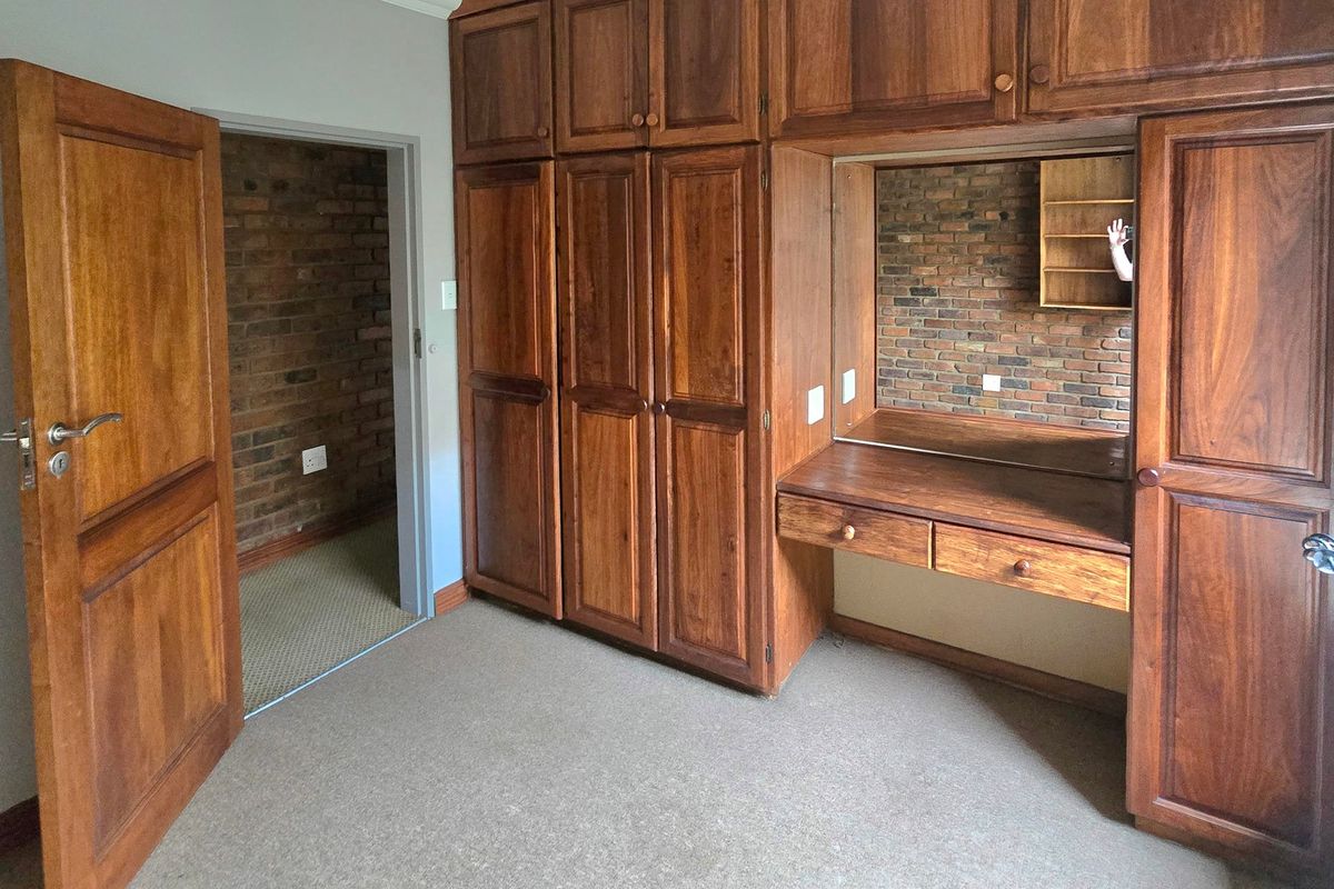 A bedroom featuring extensive built-in wooden cabinetry with an integrated vanity, exposed brick accents, and neutral carpeting.
