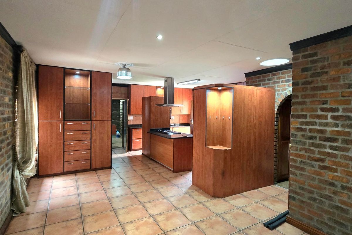 Spacious kitchen featuring extensive wooden cabinetry, a central island with a built-in hob, and rustic exposed brick accents with tiled flooring throughout.