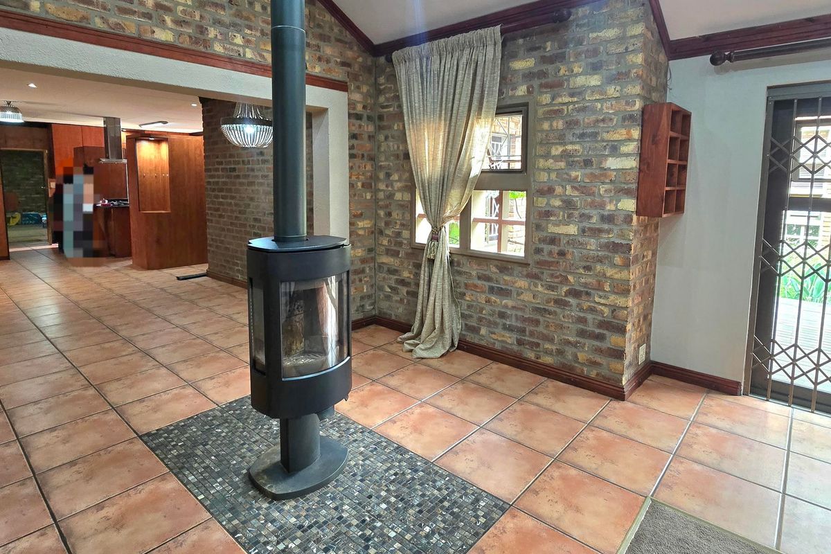 Spacious living area featuring a central freestanding fireplace, exposed brick walls, and tiled flooring with a decorative mosaic inlay.
