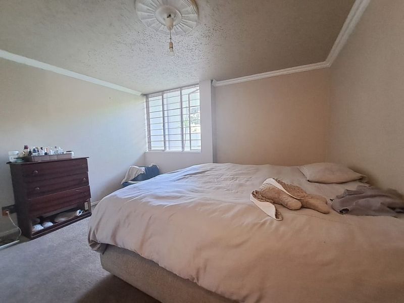 A bedroom featuring a ceiling rose, decorative cornicing, and security bars on the window. The room requires cosmetic updates to the ceiling and flooring.