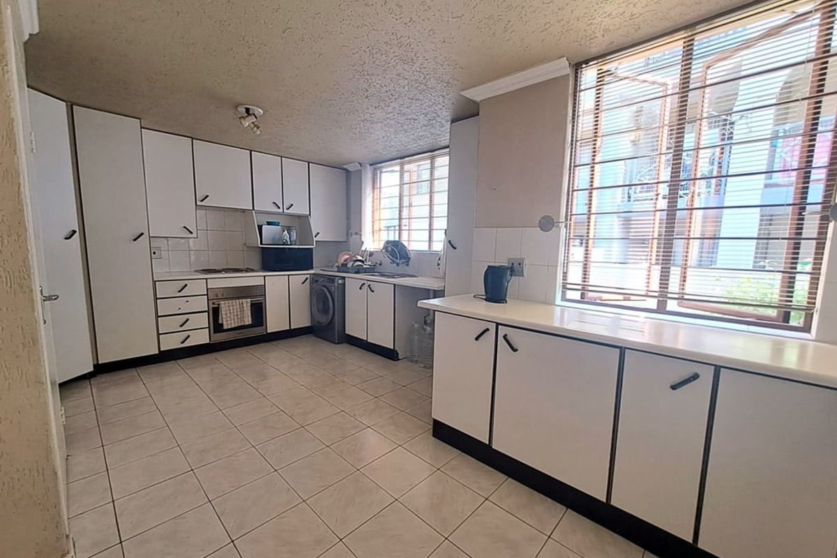 A functional kitchen featuring white built-in cabinetry, tiled flooring, integrated oven and hob, and ample natural light from large windows.