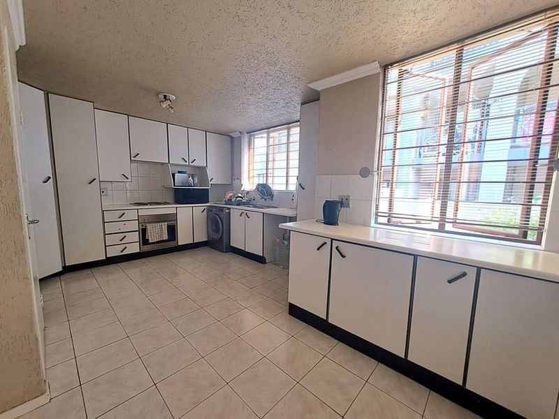 A functional kitchen featuring white built-in cabinetry, tiled flooring, integrated oven and hob, and ample natural light from large windows.