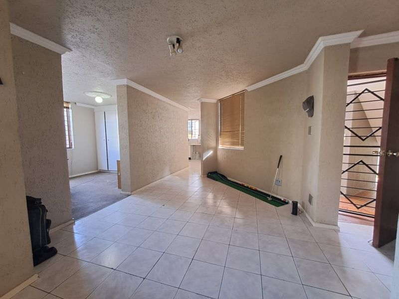 Open plan living area featuring tiled flooring, textured walls, crown molding, and a secure entrance gate, offering a versatile space for customization.