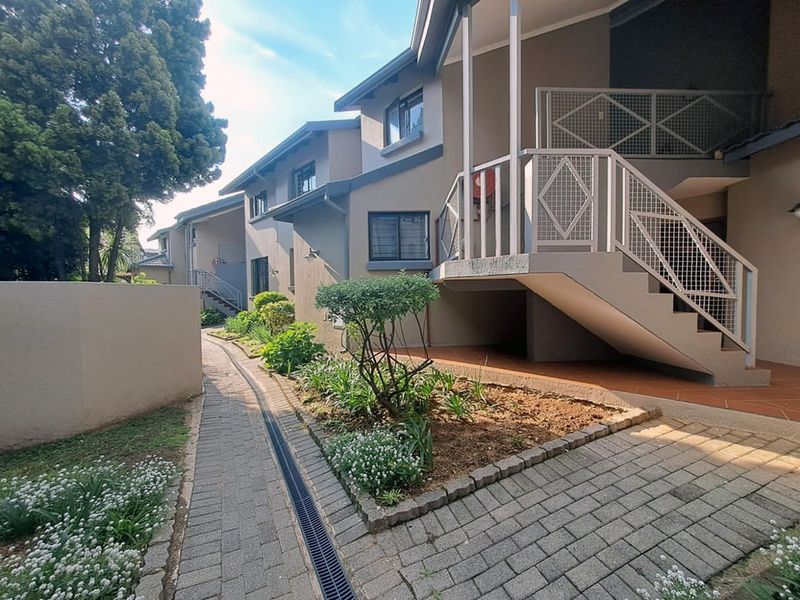 Exterior view of an apartment complex featuring a paved walkway, landscaped garden beds, and an external metal staircase leading to upper-level units.