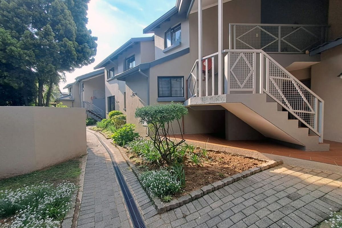 Exterior view of an apartment complex featuring a paved walkway, landscaped garden beds, and an external metal staircase leading to upper-level units.