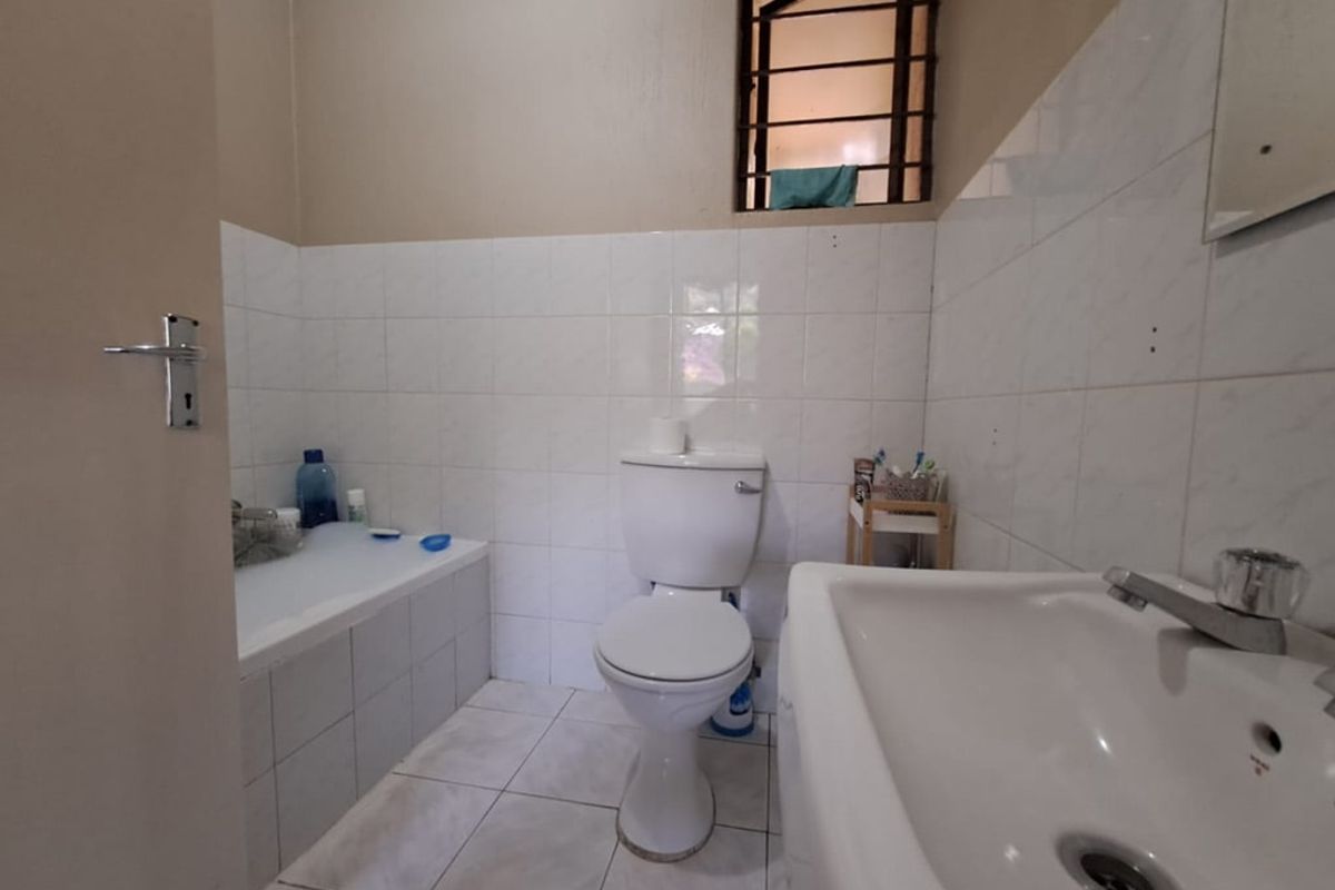 A functional bathroom featuring a bathtub, pedestal basin, and toilet with white wall tiling and tiled flooring.