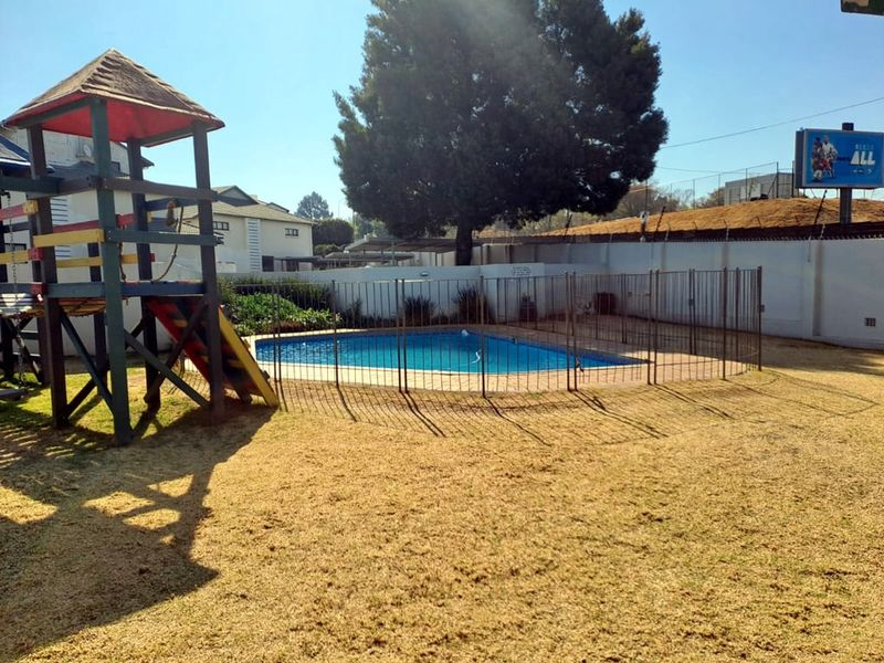 Communal outdoor area featuring a fenced swimming pool and surrounding lawn, enclosed by a perimeter wall with electric fencing.