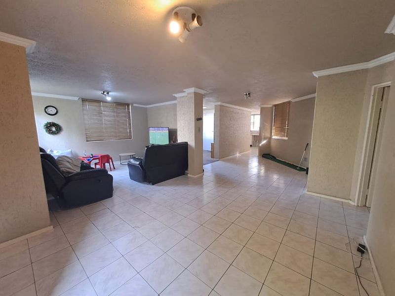 Spacious open-plan living area featuring neutral tiled flooring, structural columns, and natural light through venetian blinds.