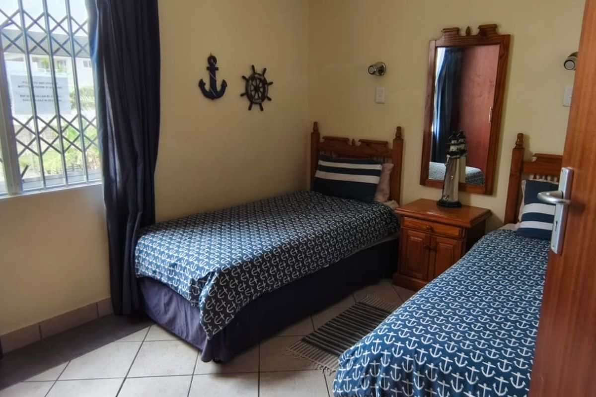 A functional bedroom featuring tiled flooring, a window with a security gate, and wall-mounted lighting fixtures.