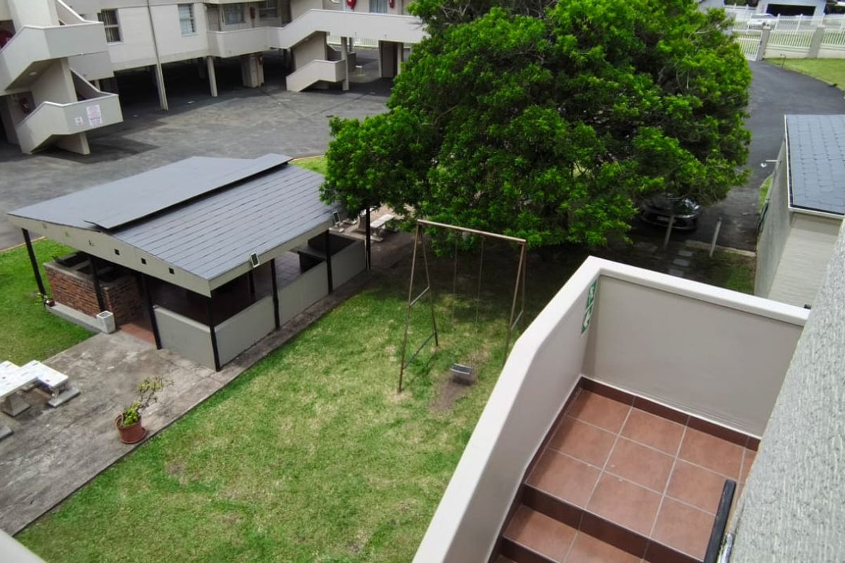 An elevated view of the apartment complex grounds, featuring a communal garden, covered braai area, and paved driveway access.