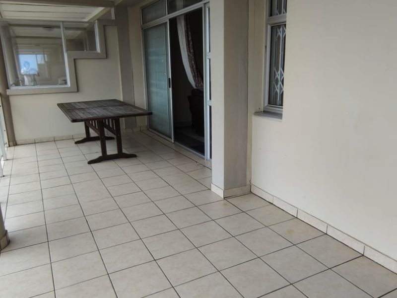 Spacious covered balcony featuring tiled flooring, glass balustrades, and sliding door access, offering an outdoor living space with coastal views.