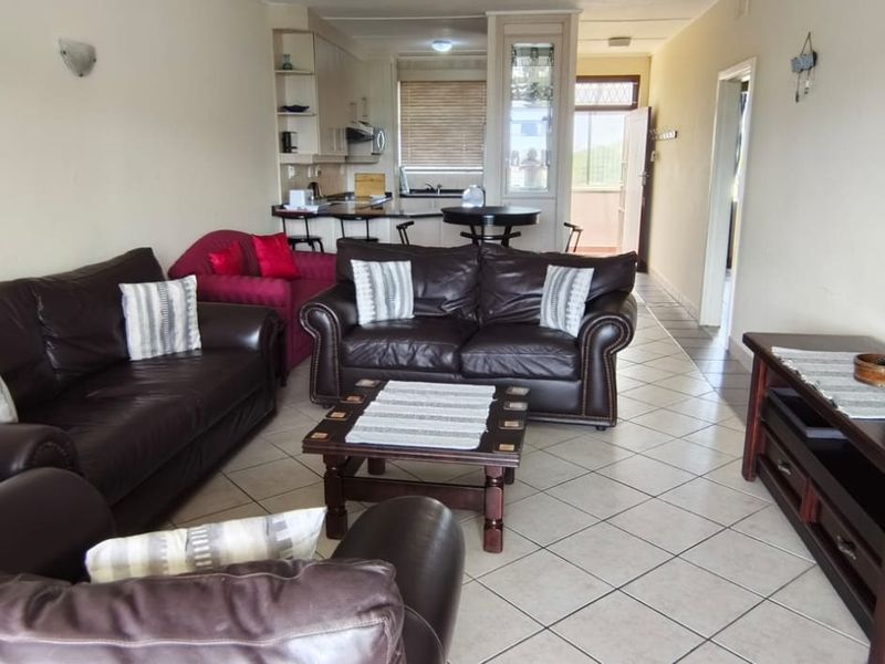 Open-plan living and kitchen area featuring tiled flooring, a breakfast bar, and functional kitchen cabinetry with built-in appliances.