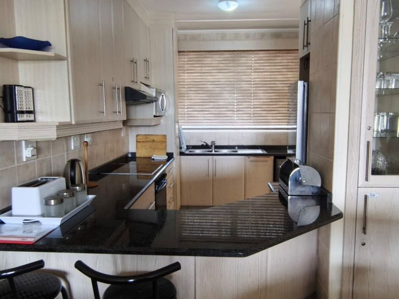 A functional kitchen featuring light wood cabinetry, dark granite countertops, a breakfast bar, and a built-in glass-front display cabinet.
