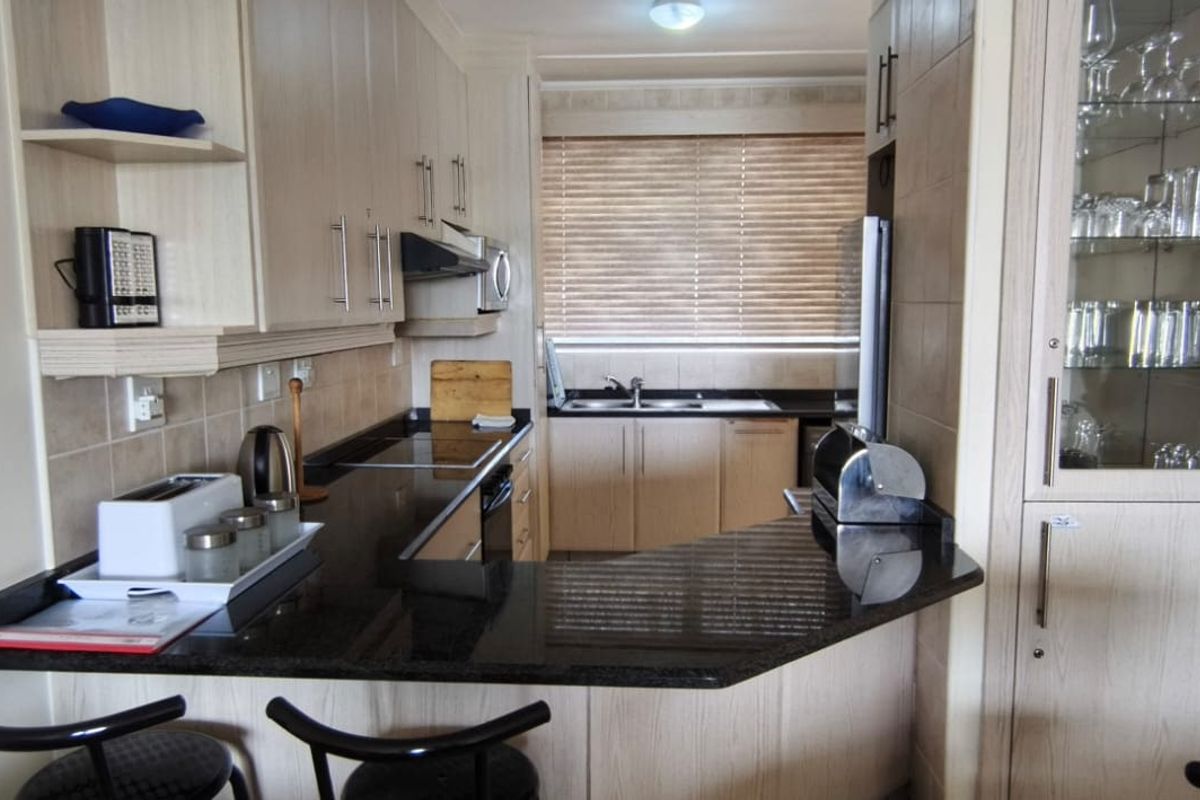 A functional kitchen featuring light wood cabinetry, dark granite countertops, a breakfast bar, and a built-in glass-front display cabinet.